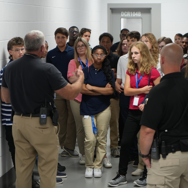 Teens listen attentively to two officers in a hallway