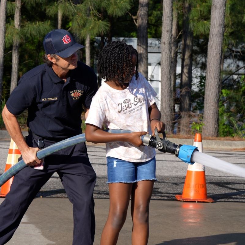 Clayton firefighter assists young girl in operating a fire hose
