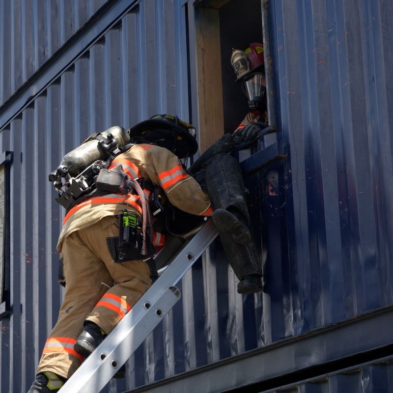 Firefighter climbs ladder to retrieve a model person from a window