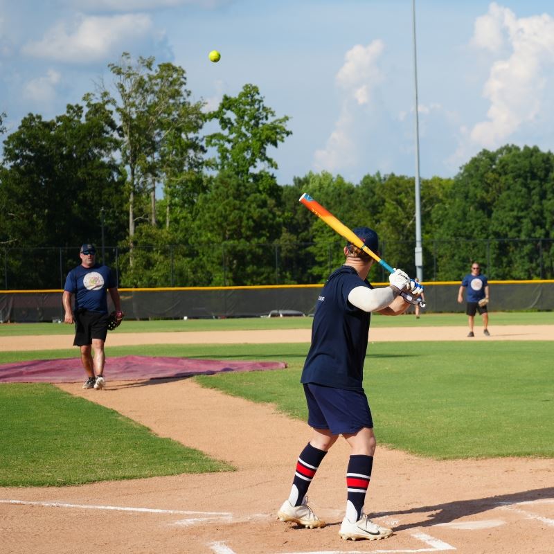 Police team member throws softball to fire team member at bat