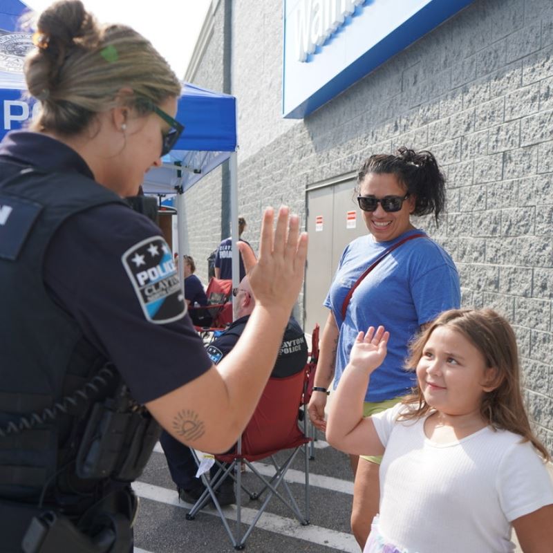 Clayton officer high fives little girl with her mom in front of Walmart at Pack a Police Car event