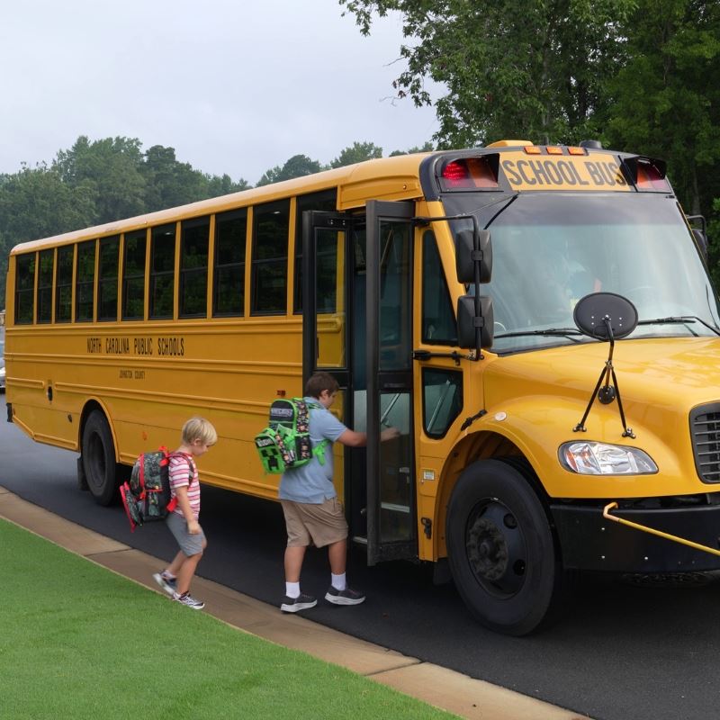 two young students with bookbags load onto school bus