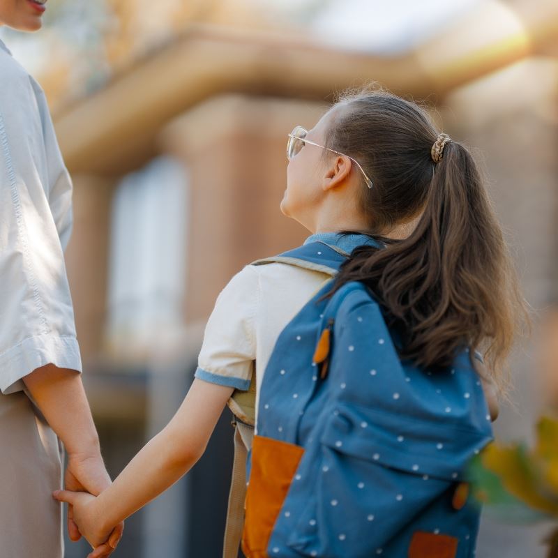 Little Girl with bookbag and glasses looks at mom